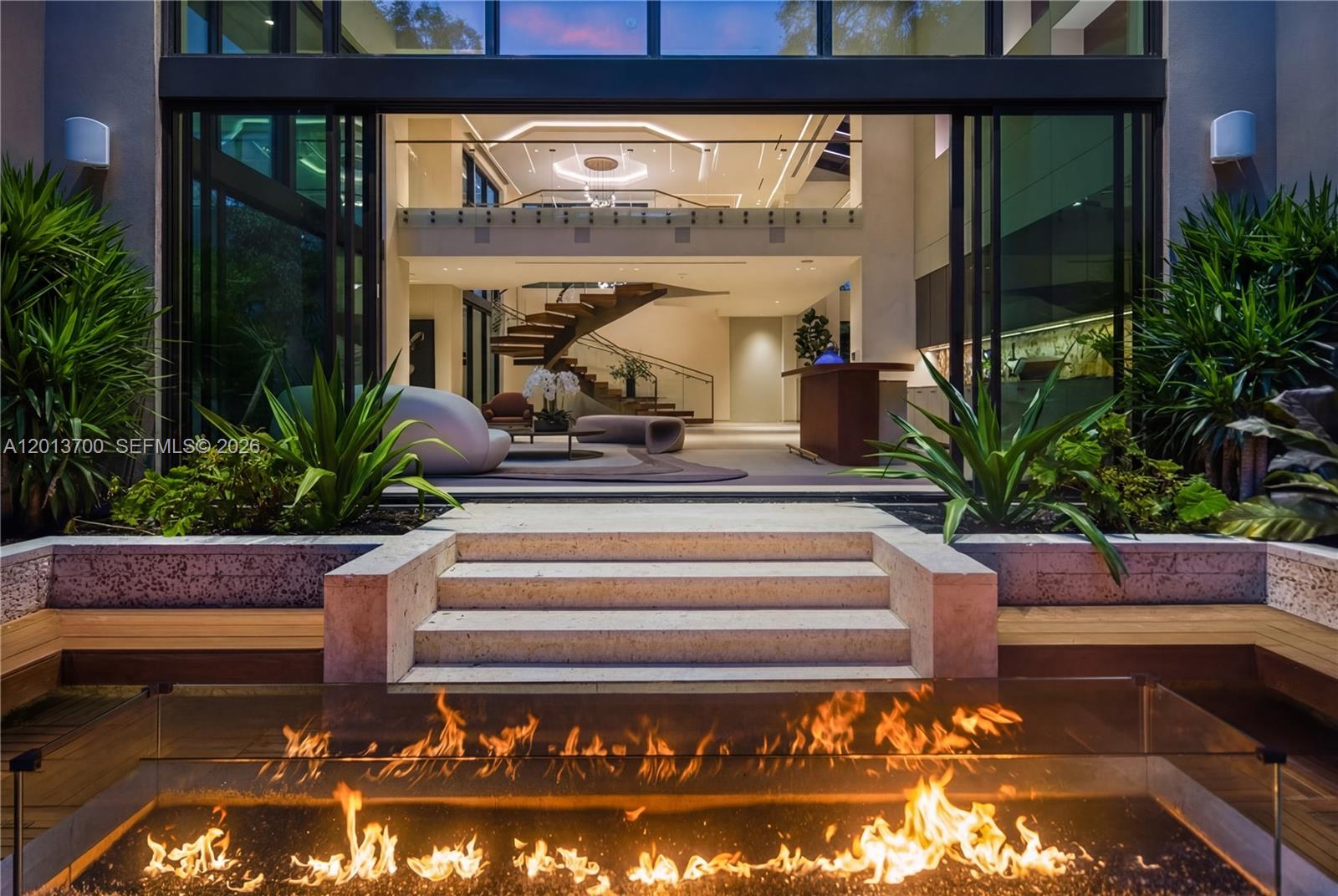 A modern home interior viewed from an outdoor patio with a glass-enclosed fire pit — 6701 SW 101st St, Pinecrest FL 33156, PINECREST, FL