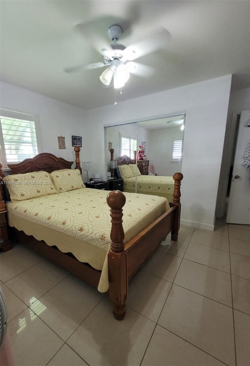 A bedroom features a wooden bed with a yellow quilt, tile floors, and mirrored closet doors — 411 S Crescent Dr # 105, Hollywood FL 33021, HOLLYWOOD, FL