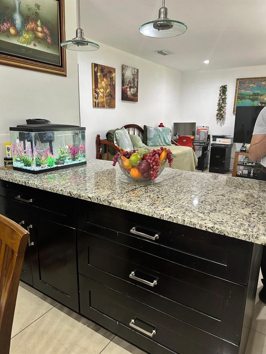 A kitchen island with dark cabinets and granite countertops sits in front of a living area — 411 S Crescent Dr # 105, Hollywood FL 33021, HOLLYWOOD, FL