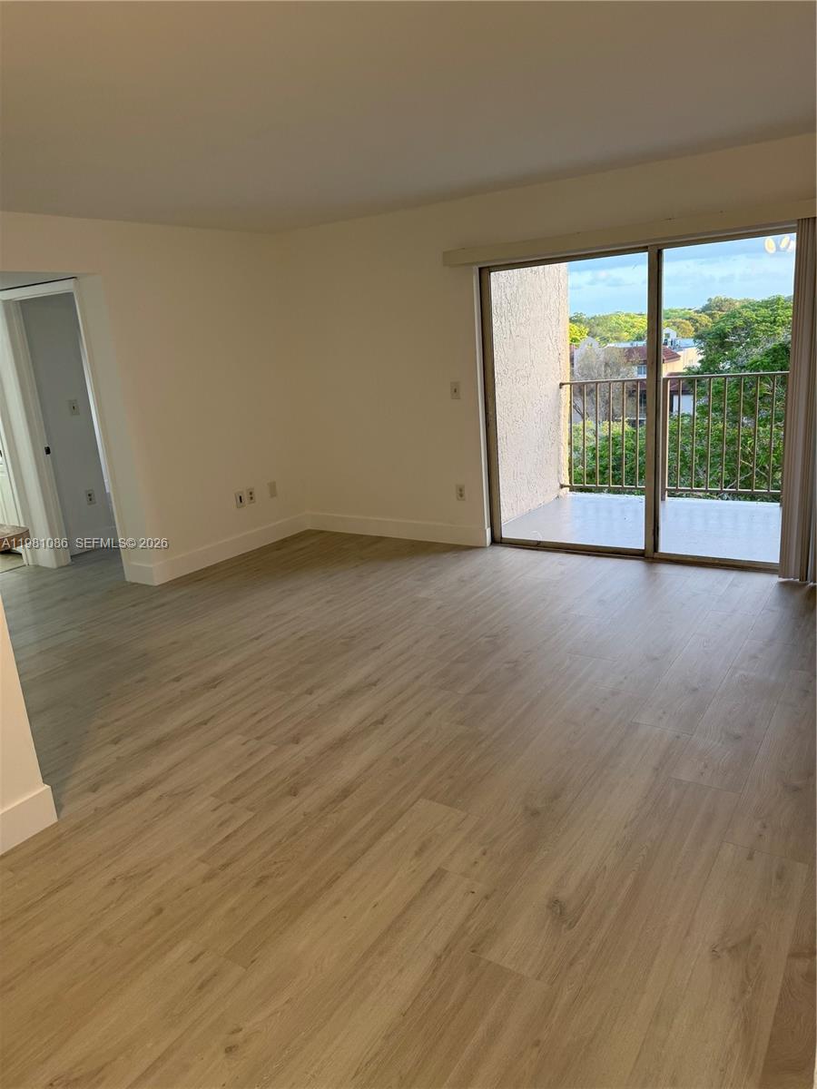 An empty living room features light wood-look flooring, white walls, and a sliding glass door — 15231 SW 80th St # 615, Miami FL 33193, MIAMI, FL