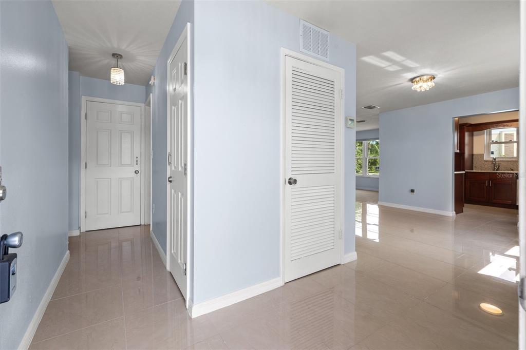 A bright entryway with light blue walls, tile flooring, and white doors leads to a kitchen — 5660 80TH STREET N UNIT A208, ST PETERSBURG, FL