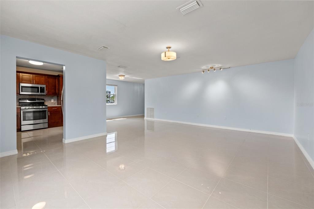 A spacious, light-blue living area with glossy tile floors leads into a kitchen with wood cabinets — 5660 80TH STREET N UNIT A208, ST PETERSBURG, FL