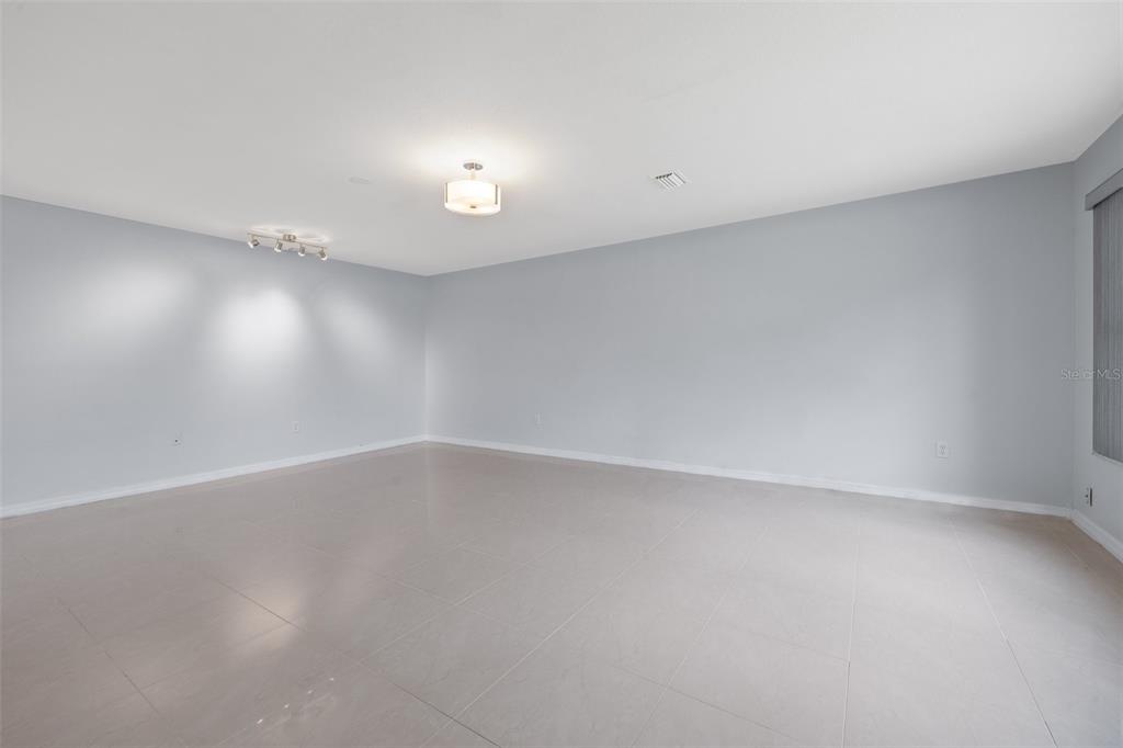 An empty room with light gray walls, large floor tiles, and two ceiling light fixtures — 5660 80TH STREET N UNIT A208, ST PETERSBURG, FL