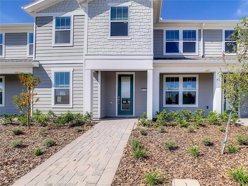 A two-story townhouse exterior features gray siding, a teal front door, and a paved walkway — 14424 ORCHID ISLAND DRIVE, ORLANDO, FL