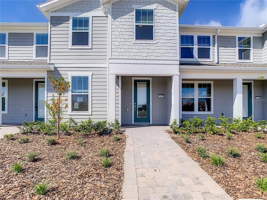 A two-story townhouse exterior features gray siding, a paved walkway, and a green front door — 14424 ORCHID ISLAND DRIVE, ORLANDO, FL