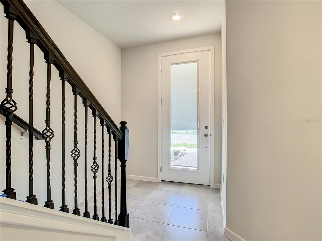 An entryway features light tile flooring, a white front door, and a black metal staircase — 14424 ORCHID ISLAND DRIVE, ORLANDO, FL