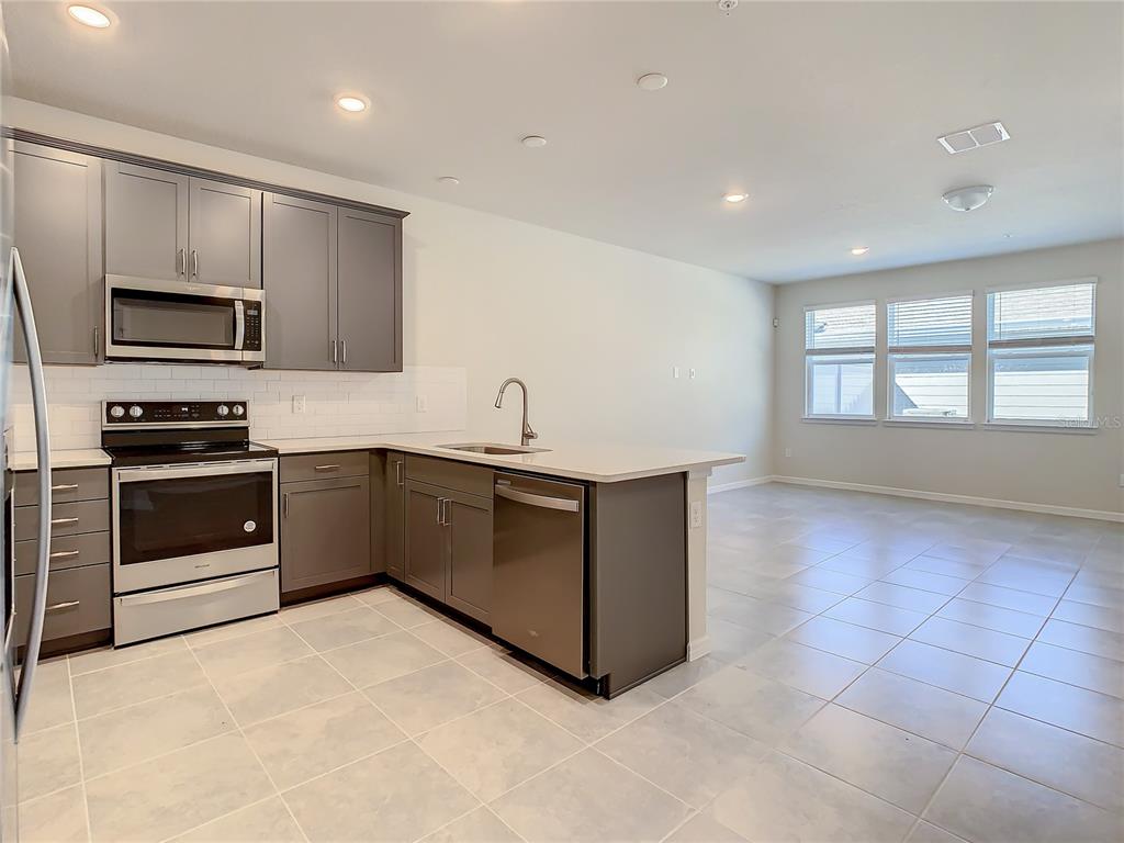 A kitchen with gray cabinets, stainless steel appliances, and tile flooring opens to a living area — 14424 ORCHID ISLAND DRIVE, ORLANDO, FL
