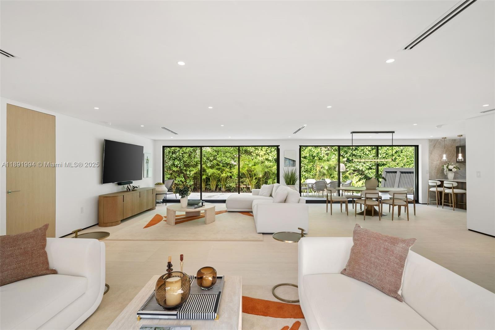 A modern, open-concept living and dining area features white furniture, large glass sliding doors, and greenery — 222 E Rivo Alto Dr, Miami Beach FL 33139, MIAMI BEACH, FL