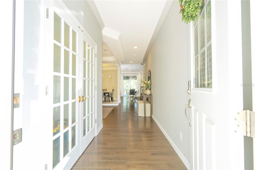 A hallway with wood-look tile flooring leads toward a dining area with French doors — 5185 DOVE TREE STREET, ORLANDO, FL
