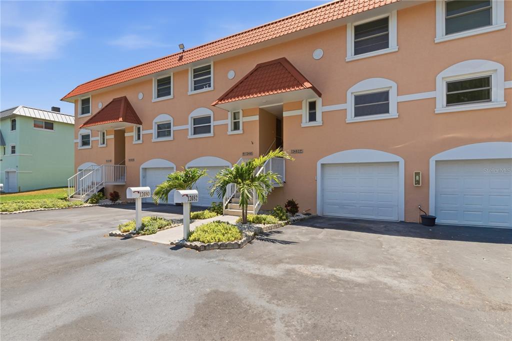 A multi-story peach-colored townhouse building with a tiled roof and several garage doors — 12482 CAPRI CIRCLE N, TREASURE ISLAND, FL