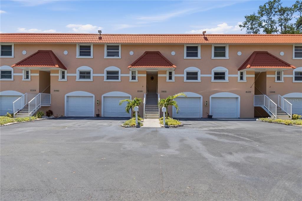 A multi-unit residential building with orange stucco walls, red tile roofs, and attached garages — 12482 CAPRI CIRCLE N, TREASURE ISLAND, FL