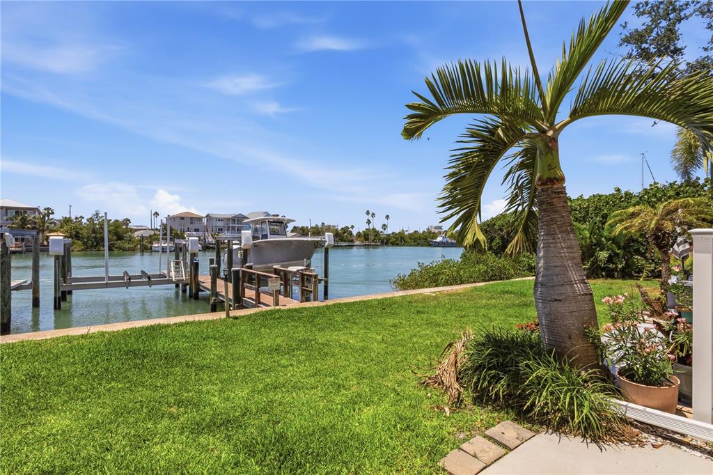 A grassy yard with a palm tree overlooks a canal with a private boat dock — 12482 CAPRI CIRCLE N, TREASURE ISLAND, FL
