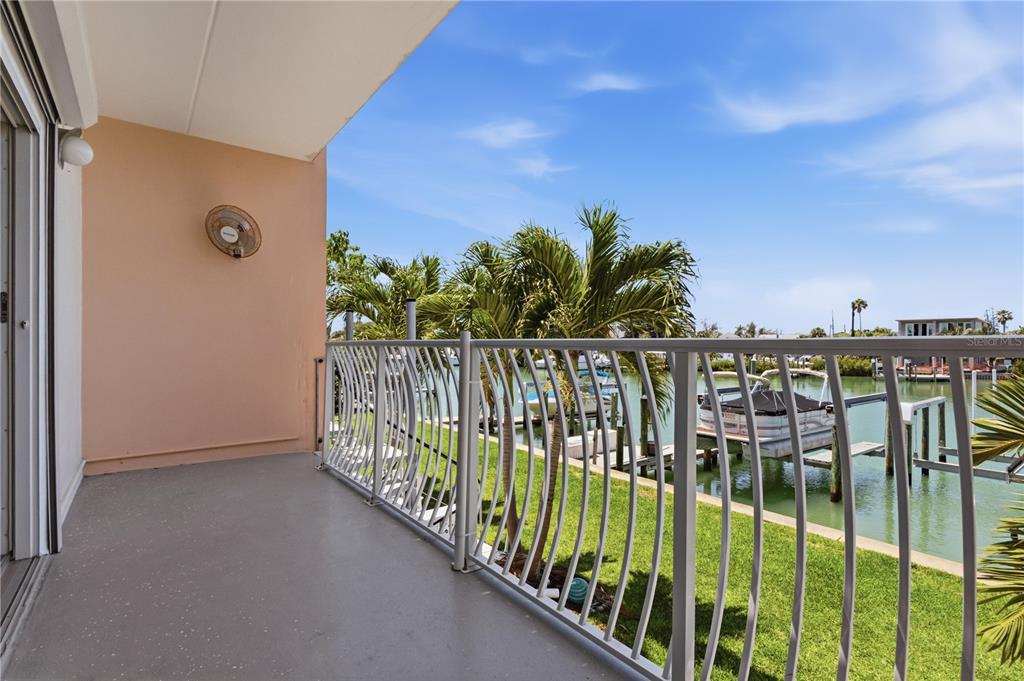 A balcony with a gray floor and white metal railing overlooks a canal with boats — 12482 CAPRI CIRCLE N, TREASURE ISLAND, FL