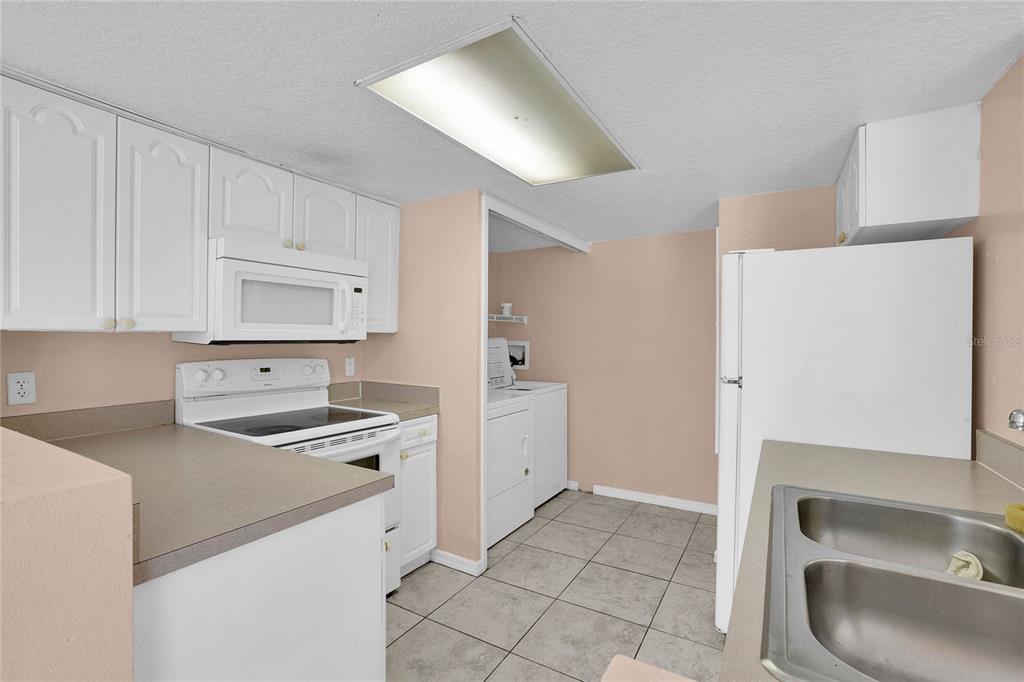 A kitchen features white cabinets, a white stove, a white refrigerator, and tiled flooring — 2918 FAN PALM DRIVE UNIT Main, DAVENPORT, FL