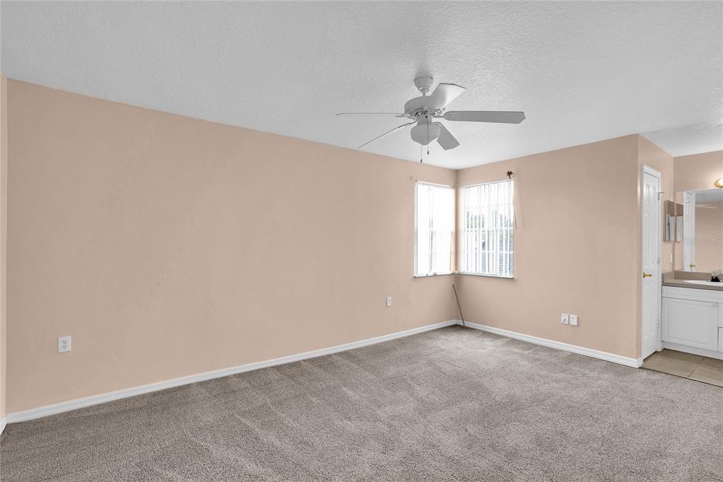 A bedroom with beige walls, gray carpeting, a ceiling fan, and an attached bathroom vanity — 2918 FAN PALM DRIVE UNIT Main, DAVENPORT, FL