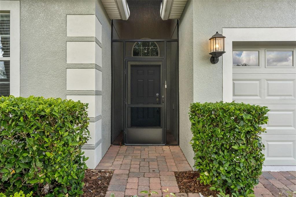 The exterior entrance features a brick walkway, a screened door, and manicured green hedges — 3859 SANIBEL STREET, CLERMONT, FL