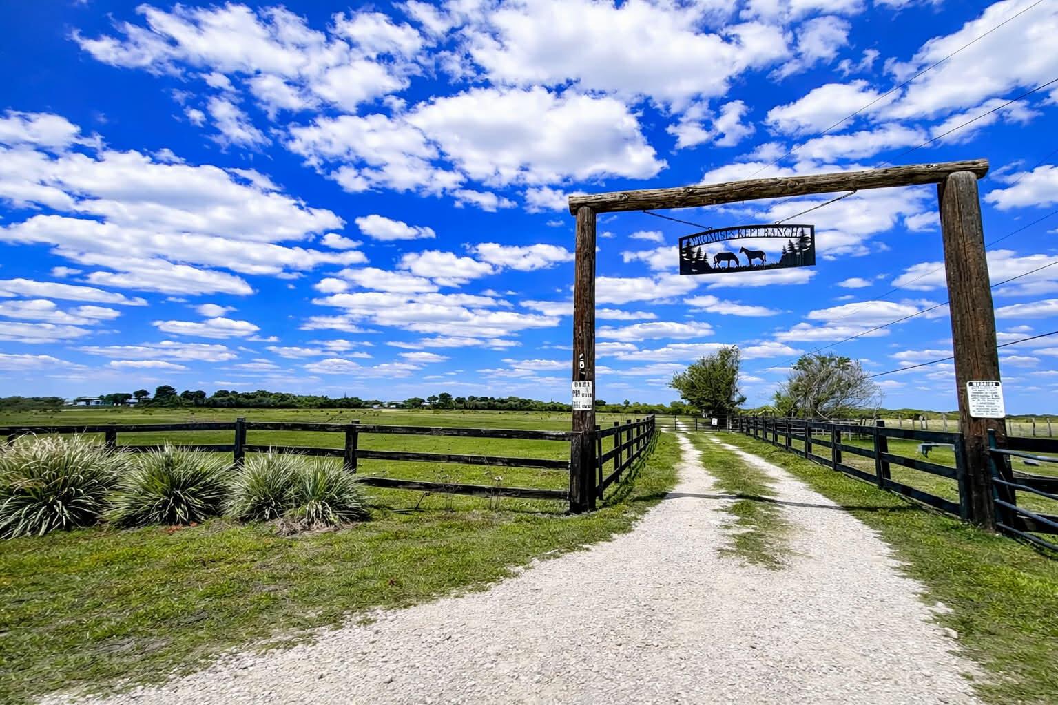 A gravel driveway leads through a wooden gate entrance into a fenced ranch property — 8121 NW 58th Lane, Okeechobee FL 34972, OKEECHOBEE, FL
