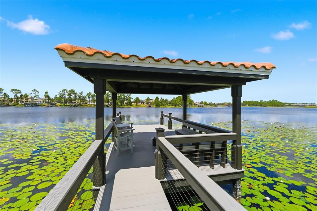A covered wooden dock with seating extends over a lake filled with lily pads — 9110 MORGANA COURT, WINTER GARDEN, FL