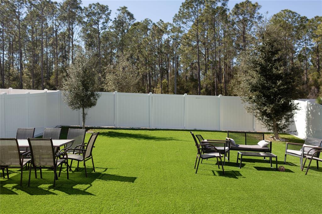 A backyard features artificial turf, a white vinyl fence, patio furniture, and two small trees — 2015 HEMINGWAY CIRCLE, GROVELAND, FL