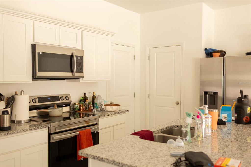 A kitchen features white cabinets, stainless steel appliances, and a granite-topped island with a sink — 2015 HEMINGWAY CIRCLE, GROVELAND, FL