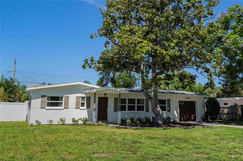 A white single-story house with a brown front door, a garage, and a large tree — 2090 76TH STREET N, ST PETERSBURG, FL