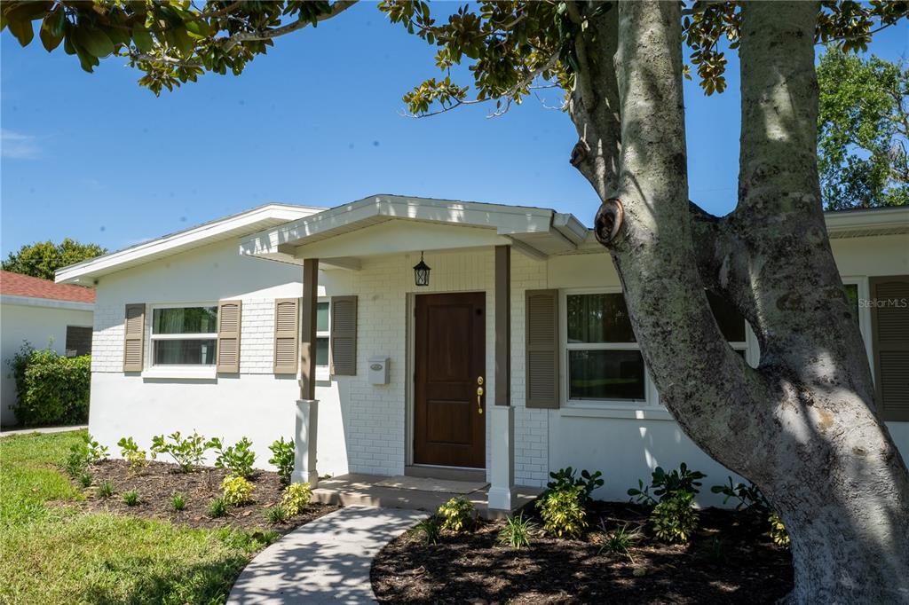 A white brick house with a wooden front door and brown shutters under a tree — 2090 76TH STREET N, ST PETERSBURG, FL