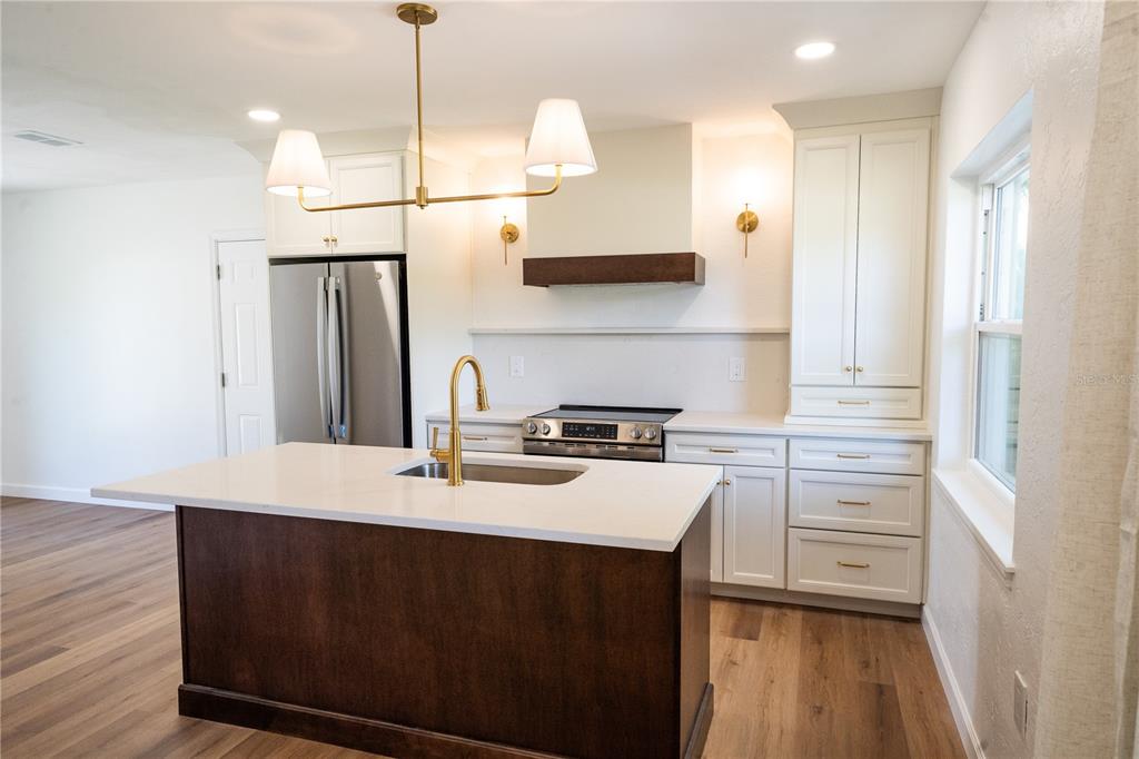 A kitchen features a dark wood island, white cabinets, stainless steel appliances, and gold fixtures — 2090 76TH STREET N, ST PETERSBURG, FL