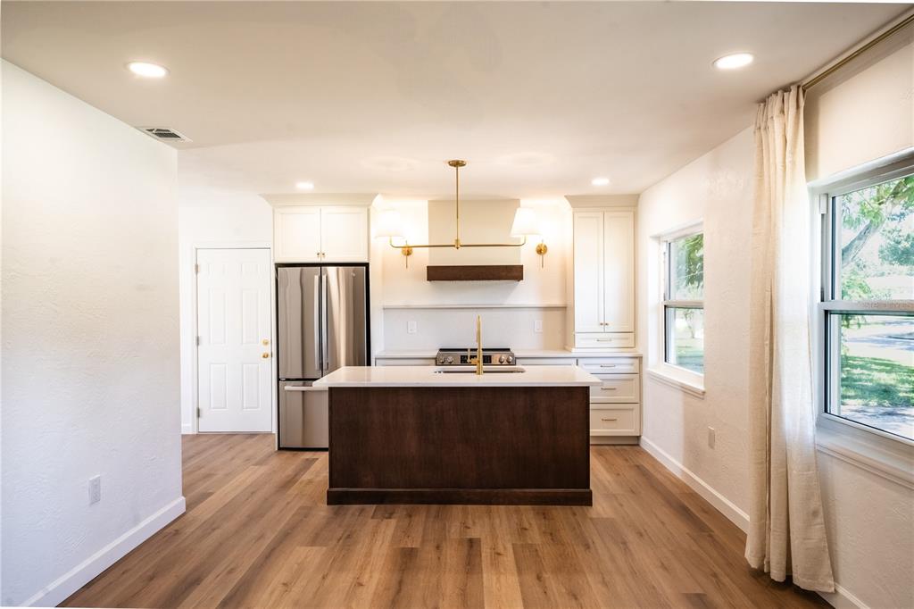 A kitchen features a dark wood island, white cabinetry, stainless steel appliances, and wood flooring — 2090 76TH STREET N, ST PETERSBURG, FL