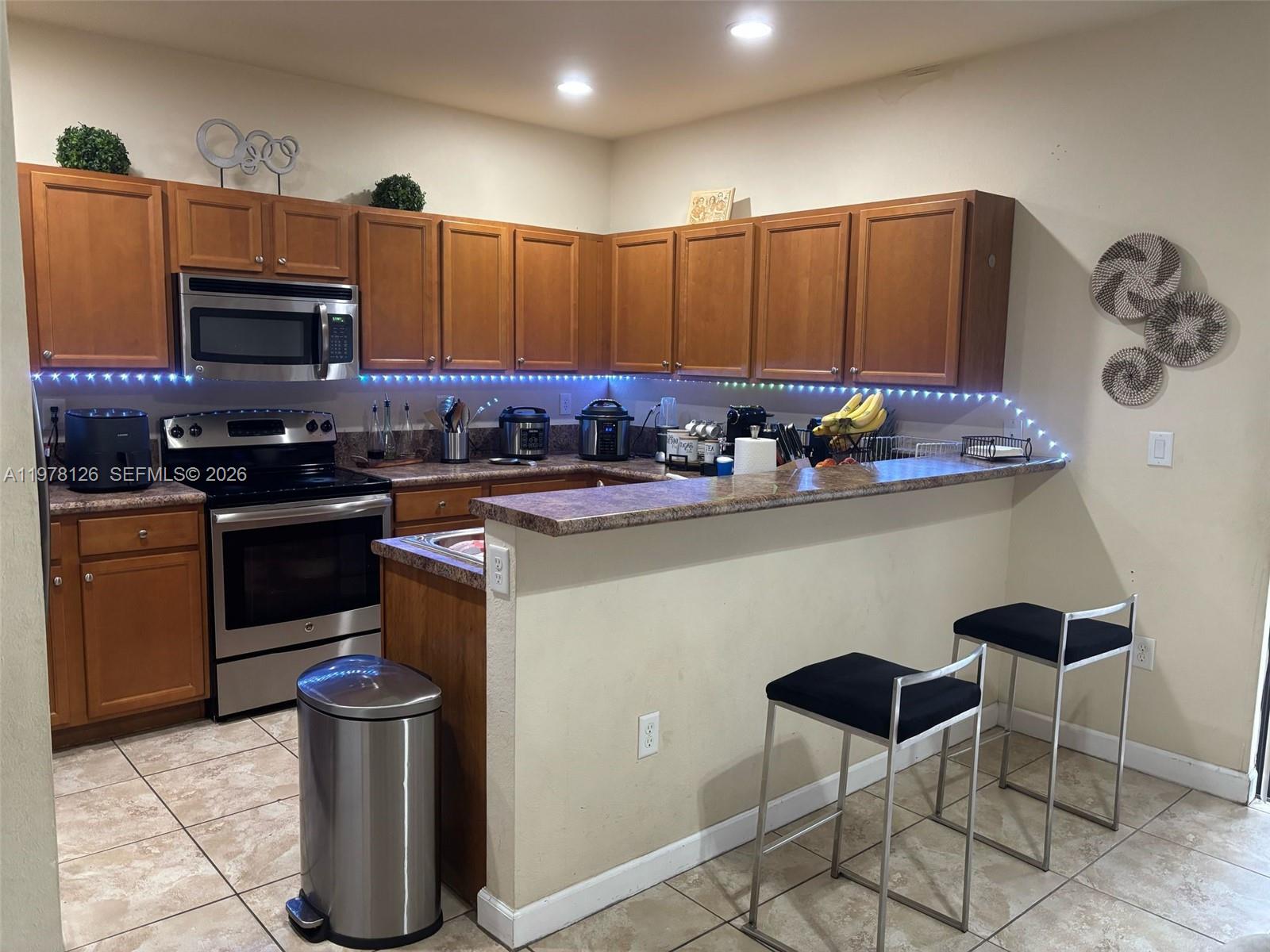 A kitchen features wood cabinets, stainless steel appliances, a breakfast bar, and two bar stools — 3544 W 88th Ter, Hialeah FL 33018, HIALEAH, FL