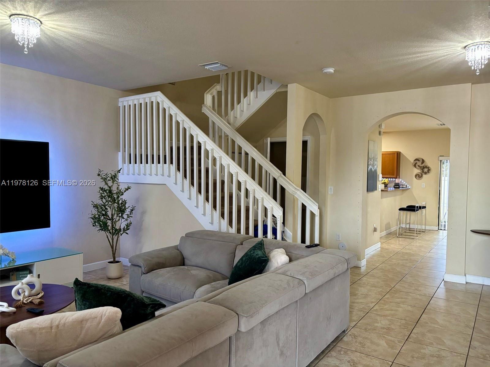 A living room features a sectional sofa, a staircase with white railings, and arched doorways — 3544 W 88th Ter, Hialeah FL 33018, HIALEAH, FL