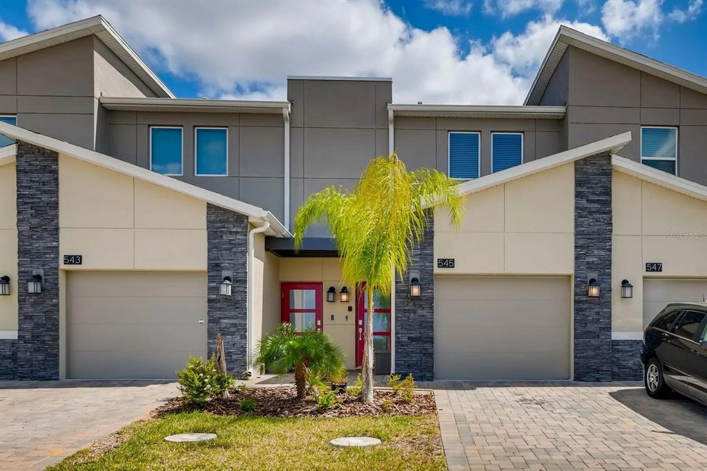 The exterior of a modern multi-unit townhouse features beige siding, stone accents, and red doors — 545 OCEAN COURSE AVENUE UNIT 545, DAVENPORT, FL
