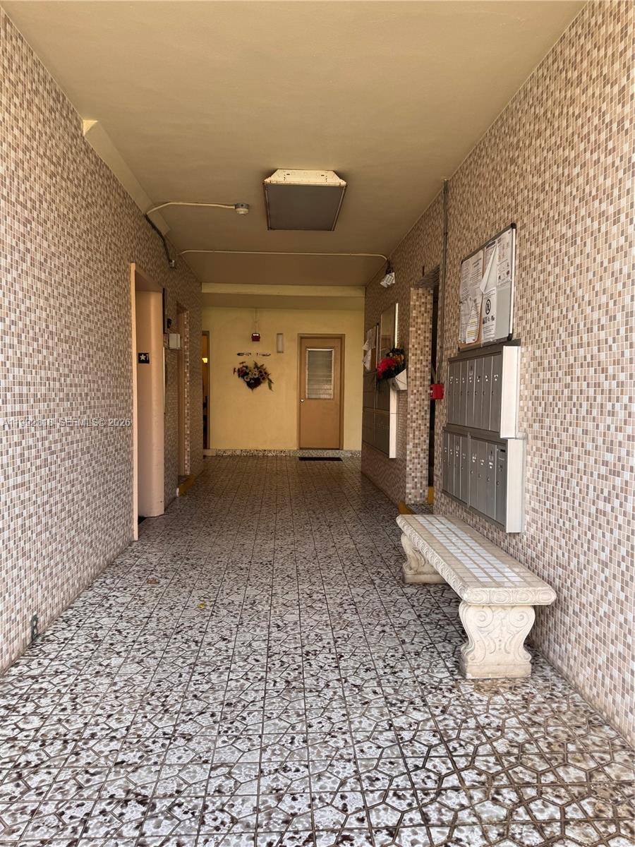 An indoor apartment building hallway features tiled walls, a tiled floor, and a stone bench — 17090 NE 14th Ave # 107, Miami FL 33162, MIAMI, FL