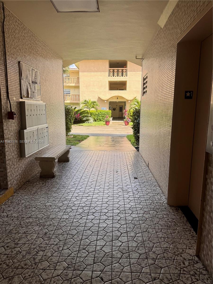 A tiled outdoor corridor features a stone bench, mailboxes, and an elevator entrance — 17090 NE 14th Ave # 107, Miami FL 33162, MIAMI, FL