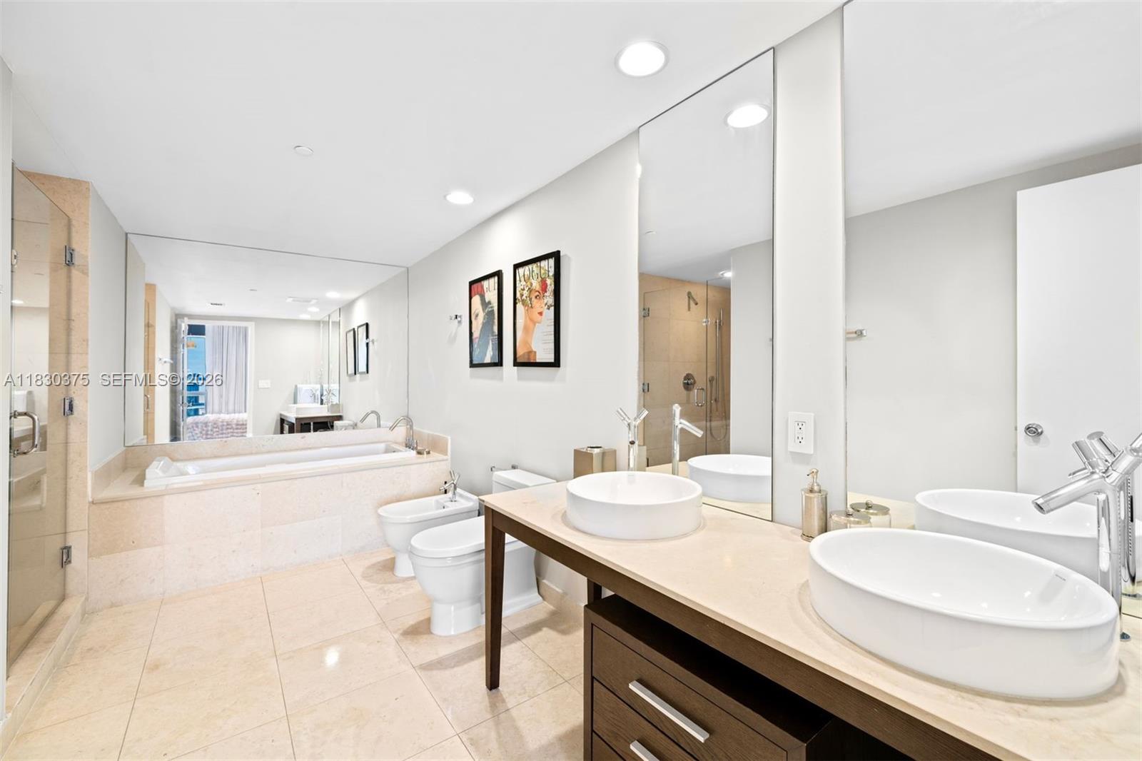 This bathroom features dual vessel sinks, a soaking tub, a bidet, and beige tile flooring — 465 Brickell Ave # 5302, Miami FL 33131, MIAMI, FL