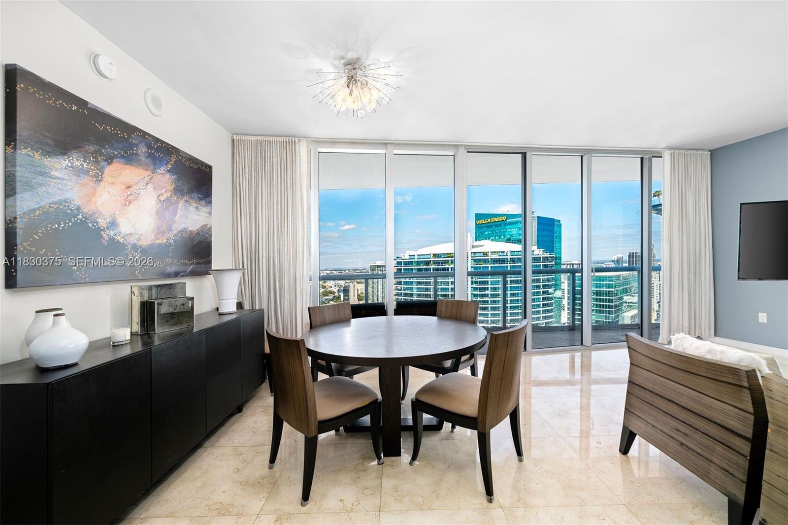 A dining room features a round table, four chairs, a black sideboard, and floor-to-ceiling windows — 465 Brickell Ave # 5302, Miami FL 33131, MIAMI, FL