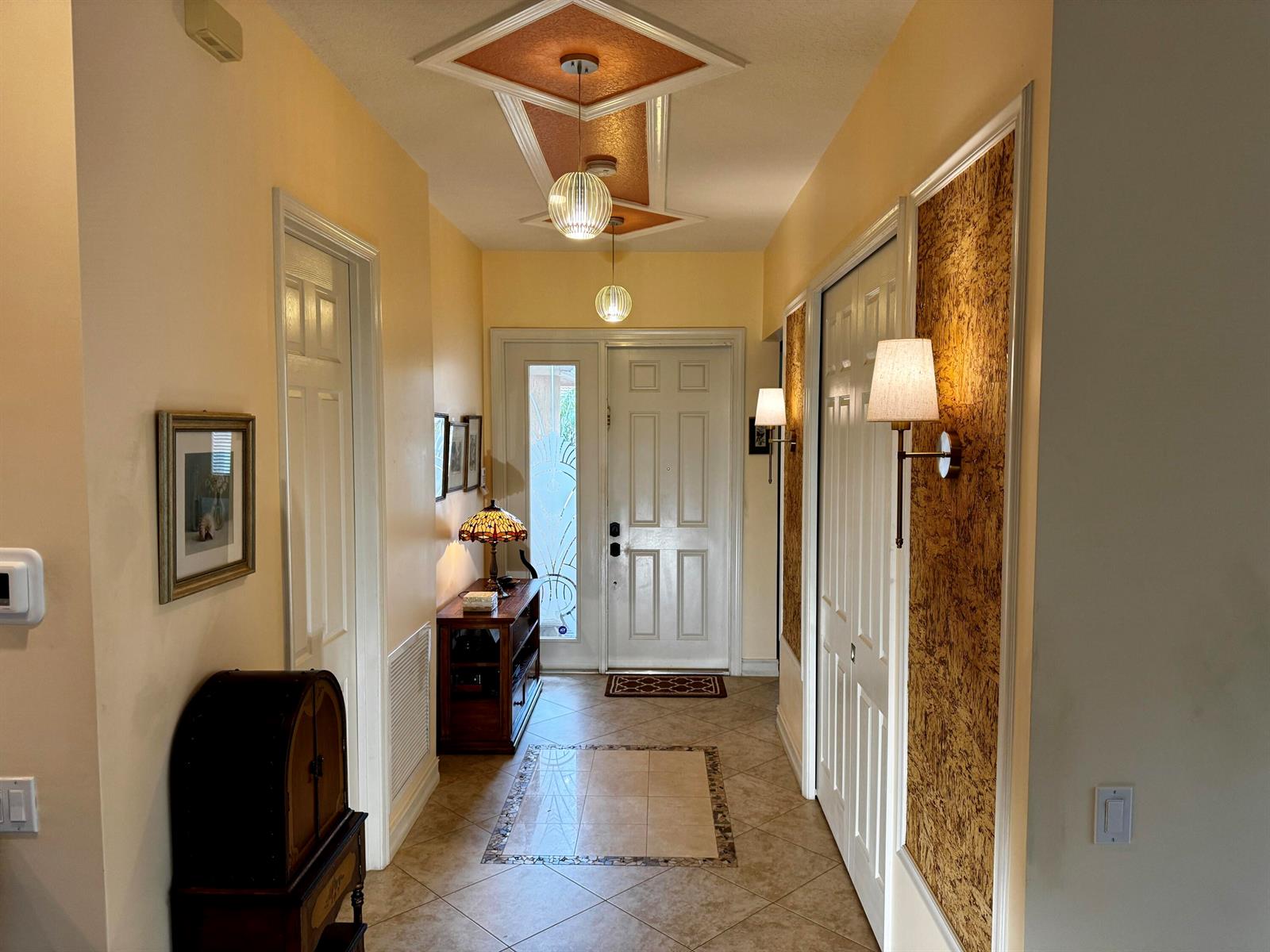 A hallway features tiled floors, a decorative ceiling inlay, and wall-mounted sconces near the entrance — 9385 Ivory Isle Road, Boynton Beach FL 33473, BOYNTON BEACH, FL
