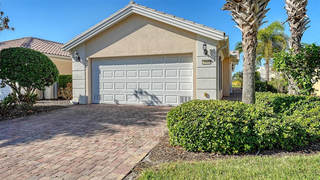 A beige house with a white garage door and a brick paver driveway — 11641 GARESSIO LANE, SARASOTA, FL