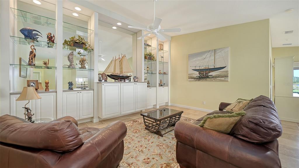 A living room features brown leather furniture, a glass coffee table, and built-in display shelving — 11641 GARESSIO LANE, SARASOTA, FL