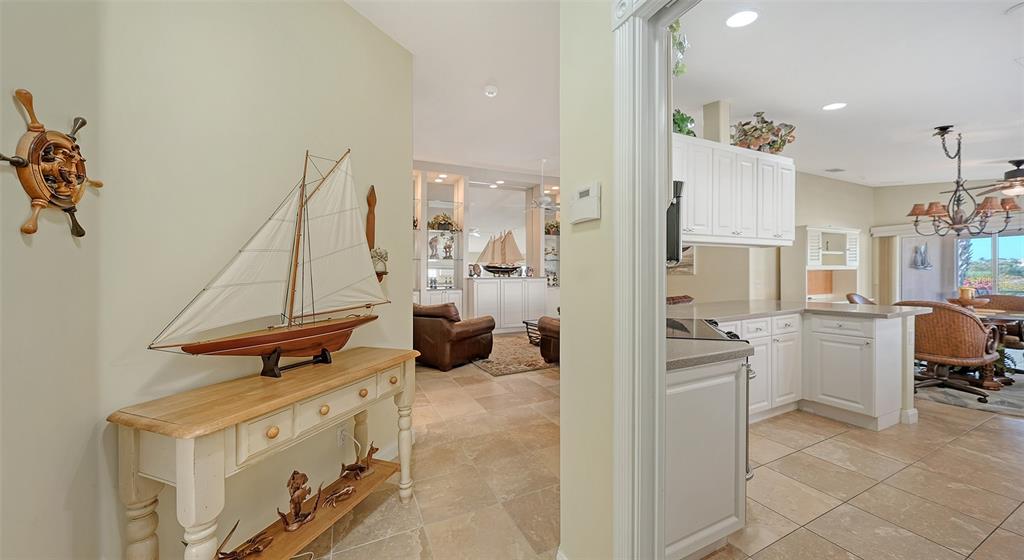 A hallway with a model sailboat leads to a kitchen and living area with tile floors — 11641 GARESSIO LANE, SARASOTA, FL
