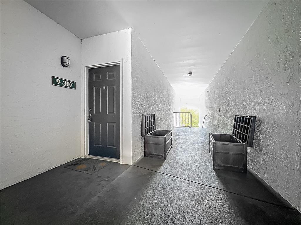 An outdoor apartment hallway features a dark door labeled 9-307 and two open storage chests — 2615 MAITLAND CROSSING WAY UNIT 9 307, ORLANDO, FL