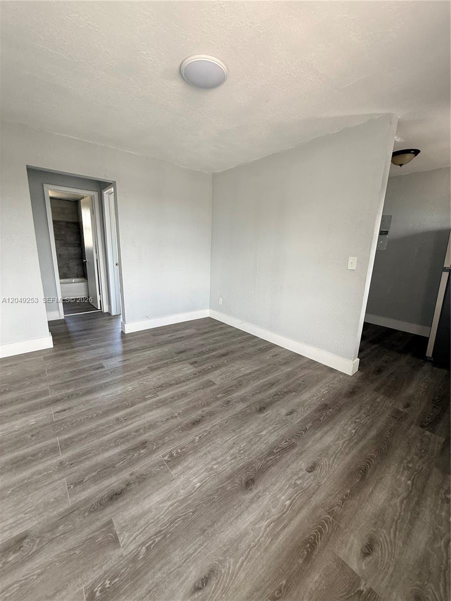 An empty room features gray walls, wood-look flooring, and a doorway leading to a bathroom — 7001 NW 15th Ave # 4, Miami FL 33147, MIAMI, FL