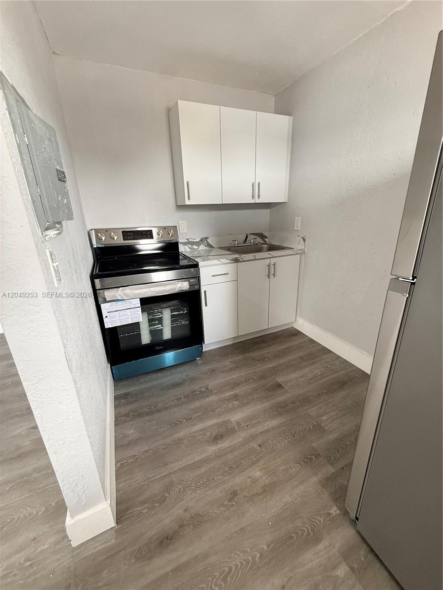 A small kitchen features white cabinets, a black electric stove, and wood-look flooring — 7001 NW 15th Ave # 4, Miami FL 33147, MIAMI, FL