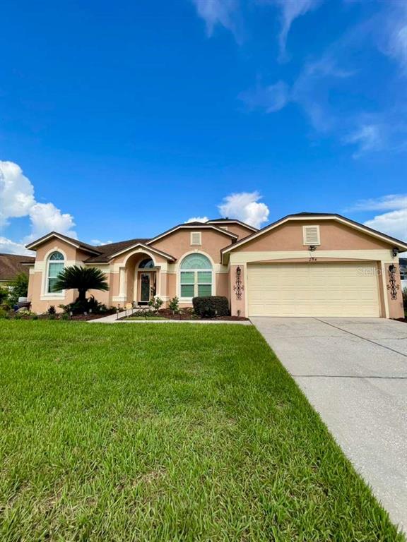 A single-story tan stucco house with a two-car garage and a front lawn — 254 LOMA DEL SOL DRIVE, DAVENPORT, FL
