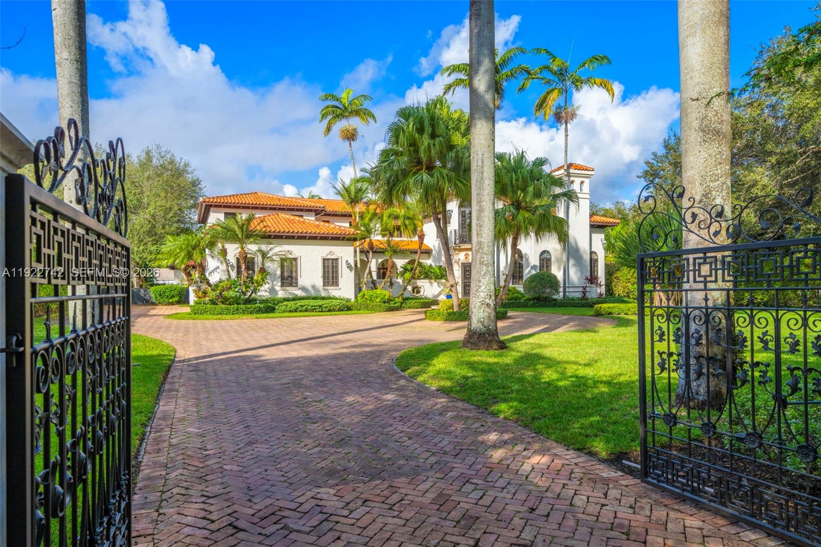 A large Mediterranean-style house with a brick driveway and palm trees behind an iron gate — 8800 SW 57 Ave, Pinecrest FL 33156, PINECREST, FL