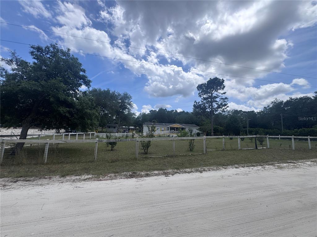A white fence encloses a yard with a house and trees under a cloudy sky — 21170 SE 67TH PLACE, MORRISTON, FL