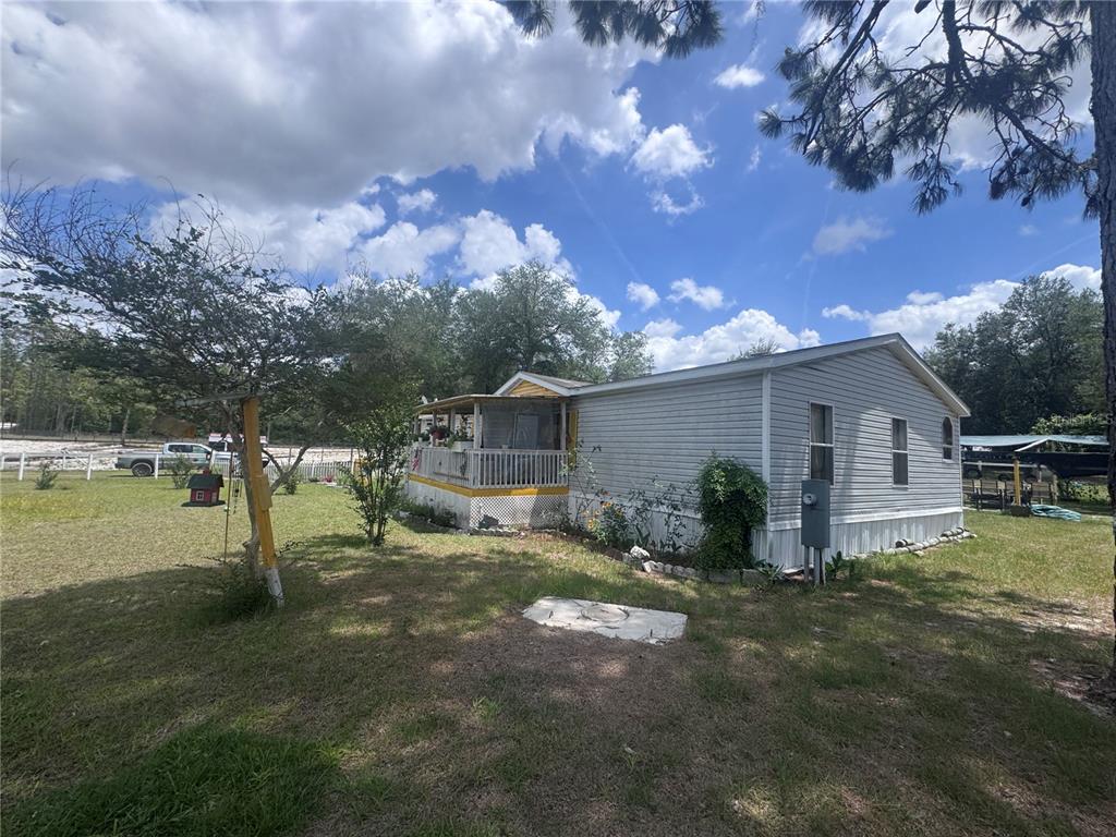 A light-colored mobile home with a covered front porch sits on a grassy lot — 21170 SE 67TH PLACE, MORRISTON, FL