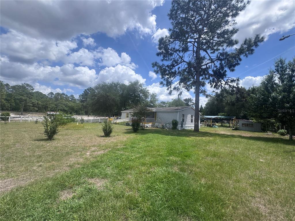 A single-story manufactured home sits on a large, grassy lot with scattered trees — 21170 SE 67TH PLACE, MORRISTON, FL