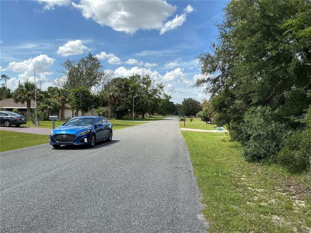 A blue sedan is parked on a residential street lined with trees and houses — MARION OAKS DRIVE, OCALA, FL