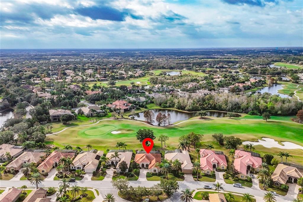 An aerial view shows a residential street with houses bordering a golf course and lake — 7042 VILAMOURA PLACE, LAKEWOOD RANCH, FL