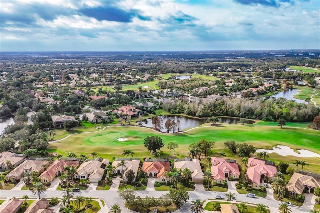 An aerial view shows a residential neighborhood with houses bordering a golf course and lake — 7042 VILAMOURA PLACE, LAKEWOOD RANCH, FL